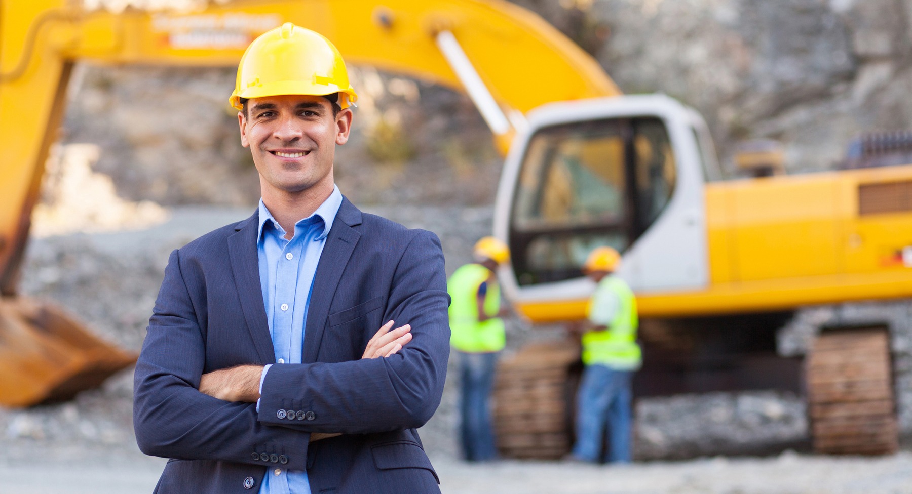 Man in business suit with hard hat standing in front of heavy equipment