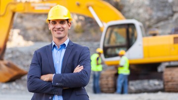 Man in suit and hard hat standing in front of excavator